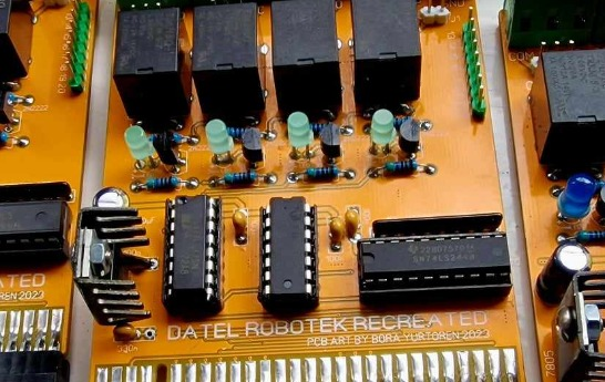 Close-up of an assembled Datel Robotek recreation board: an orange PCB with four relays, LEDs, and through-hole logic ICs, silkscreened 'DATEL ROBOTEK RECREATED'
