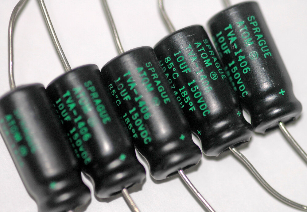Five black axial electrolytic capacitors lined up, with wire leads coming out of both ends of each one