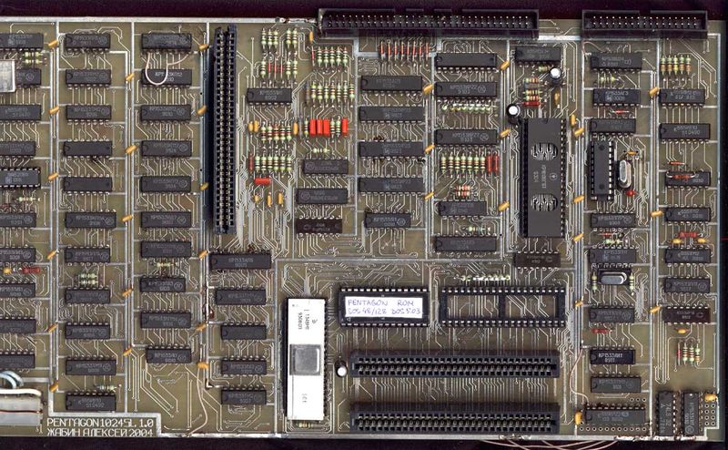 A hand-built Pentagon-1024SL circuit board: rows of Soviet-era chips with Cyrillic markings, hand-soldered bridge wires, and a hand-written label reading PENTAGON ROM stuck to one of the chips