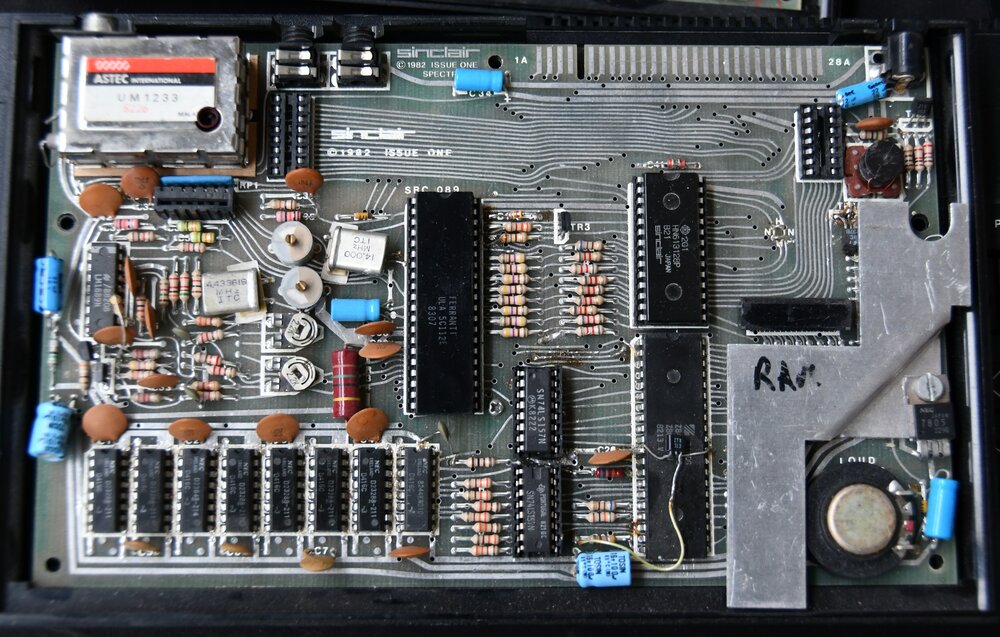 Close-up interior photo of a Sinclair ZX Spectrum Issue One motherboard from 1982, showing rows of resistors and RAM chips, a hand-written RAM label, and a black integrated circuit near the centre of the board marked FERRANTI ULA 5C1